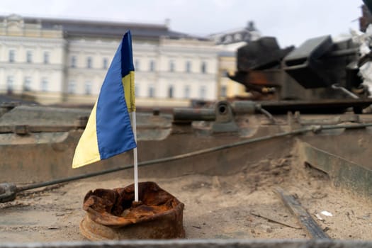 The Ukrainian flag against the background of destroyed military equipment, a tank, a concept on the theme of war and defense, the liberation of Ukrainian territories from occupation.