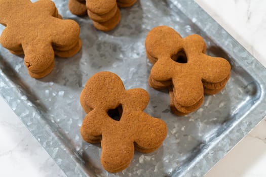 Gingerbread cookies, including a gingerbread man with a heart-shaped cutout, rest on a rustic metal tray against a marble countertop.