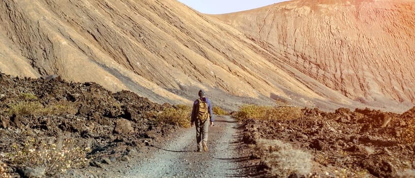 A young man leads an active lifestyle, traveling through the valley, hiking among picturesque sand mountains and volcanoes in the desert with a backpack.