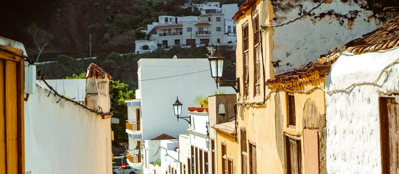 A beautiful picturesque street of the old town in the sun, houses with yellow and white walls, vintage windows and street lamps in a small village among the mountains.