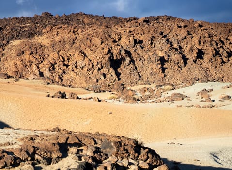Volcanic lunar landscape in the sun with black lava formations, mountains and desert, red golden sand. Scenic dramatic view with volcanoes and rocks at sunset.