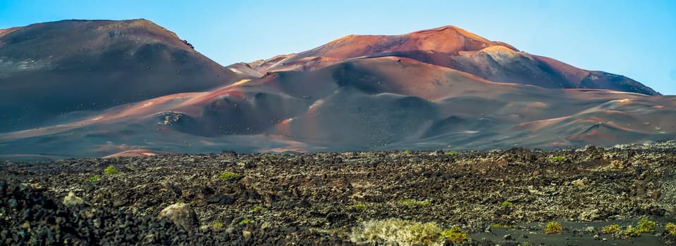 Volcanic landscape with fossilized dark lava, stones, rocks, mountains and volcanoes in Lanzarote National Park, Canary Islands.