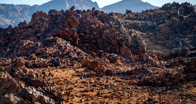 Volcanic lunar landscape in the sun with black lava formations, mountains and desert, red golden sand. Scenic dramatic view with volcanoes and rocks at sunset.