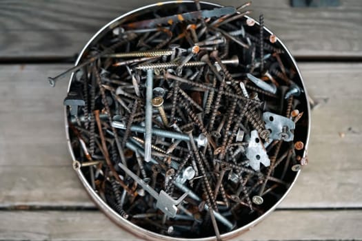 Old vintage nails in a round box lie on the porch of a wooden country house, top view. Old things for workshop and recycling and creative work.