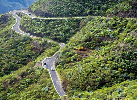A picturesque serpentine asphalt road among mountains and hills with tropical forest on the islands of the Atlantic Ocean on a sunny day, view from above.