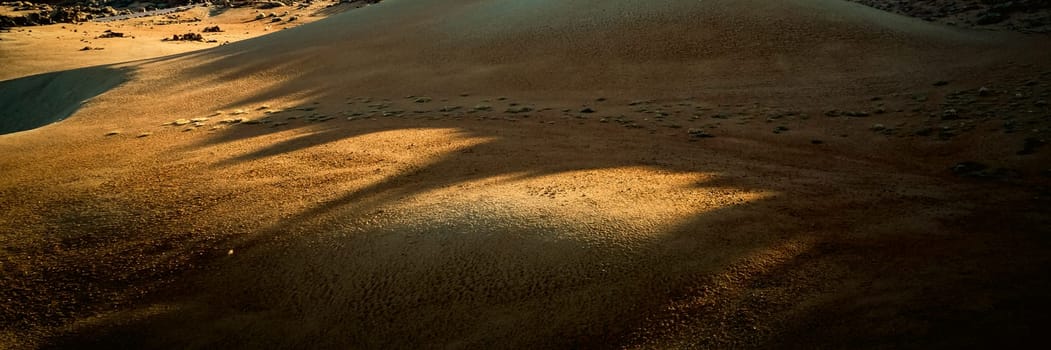 Majestic desert with yellow sand among mountains, rocks, volcanic landscape in the rays of the sun.