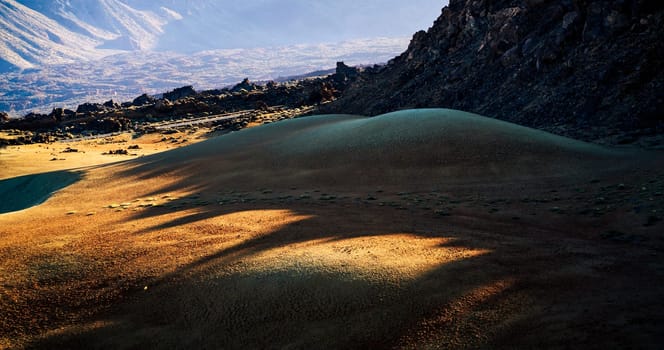 Majestic desert with yellow sand among mountains, rocks, volcanic landscape in the rays of the sun.