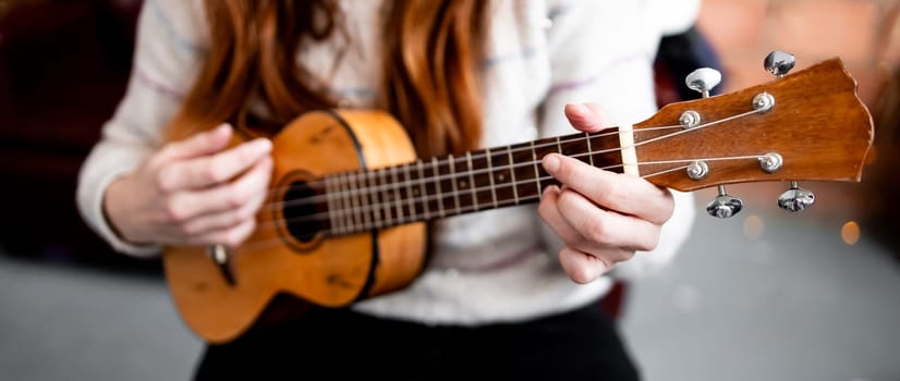 Female adult playing acoustic ukulele indoors.
