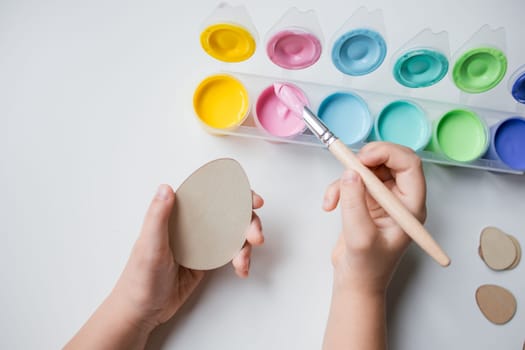 Child painting Easter egg with pastel colors on white background.