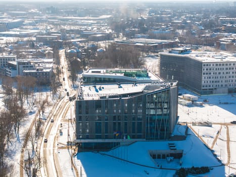 Aerial view of Riga, Latvia, showcasing the modern University of Latvia building with glass facades, snow covered streets, and a sprawling cityscape.