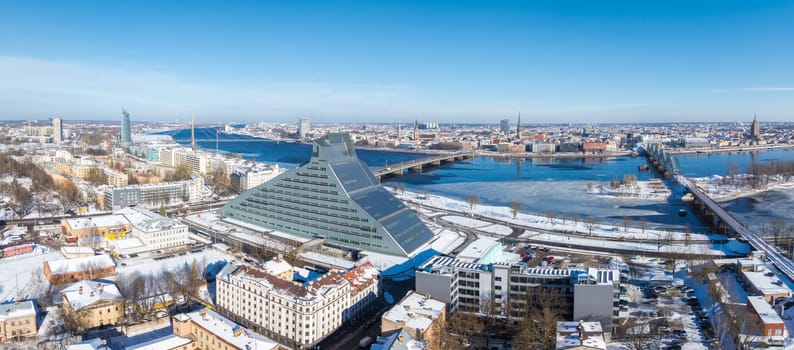 Snow covered rooftops and streets in Riga, Latvia, with the National Library in the foreground, the Daugava River, and Old Town spires in the background.