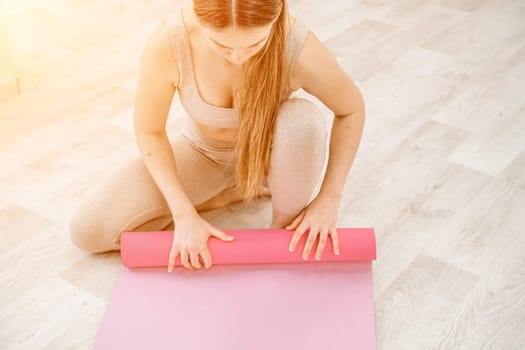 A young woman rolls a pink fitness or yoga mat before or after exercising, exercising at home in the living room or in a yoga studio. Healthy habits, keep fit, weight loss concept. Closeup photo.