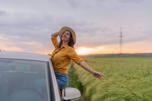 A woman is sitting in a car with her hat on and smiling. The sun is setting in the background