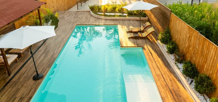 Modern backyard with turquoise swimming pool, wooden deck, umbrellas, and lounge chairs in a serene setting