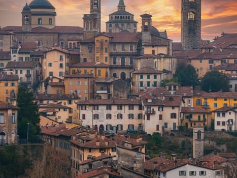 View of Bergamo's old town in Italy during sunset, featuring the Basilica of Santa Maria Maggiore, Campanone bell tower, and terracotta roofed buildings.