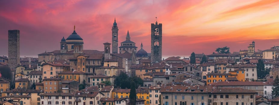 The old town of Bergamo, Italy, at sunset, featuring the Basilica of Santa Maria Maggiore, the Campanone, and terracotta roofed buildings.