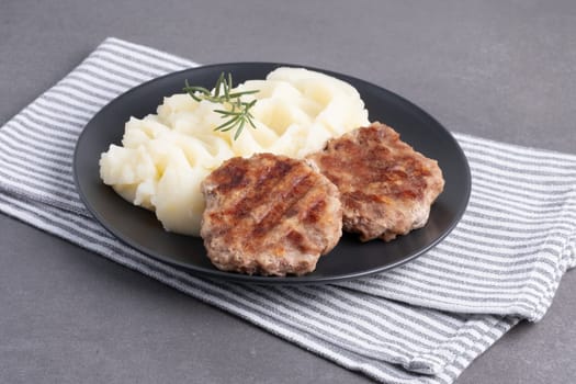 Savory grilled patties with creamy mashed potatoes and fresh rosemary on a dark plate.