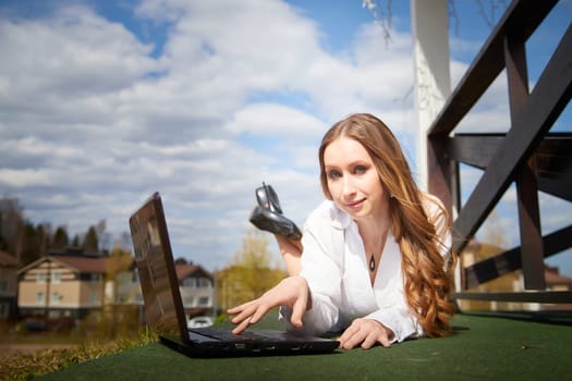 A woman is lying on the ground using a laptop, enjoying the sunny weather in a urban setting.