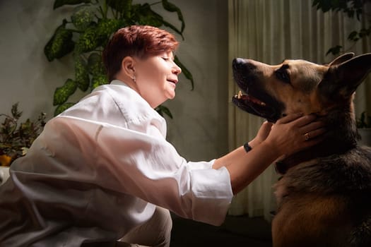 In a cozy room, a middle-aged woman shares a warm bond with her German Shepherd, embracing her pet lovingly.