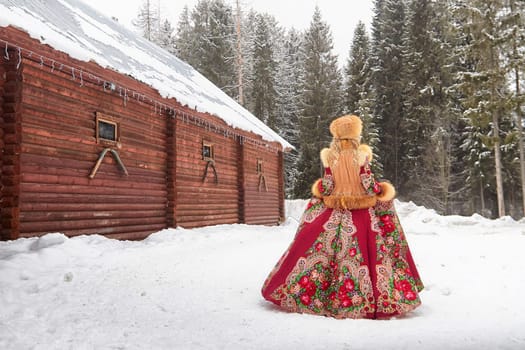 A beautiful girl in vibrant national dress poses with a horse during Maslenitsa celebrations in a winter landscape.