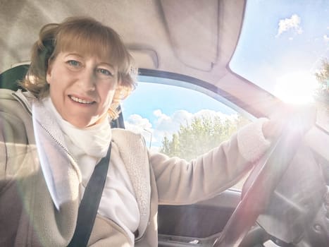 Middle-aged woman smiles while driving her car on a bright day during a travel adventure filled with excitement.