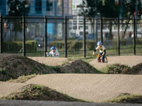 Dirt bike trail and child on bike at background. Pump track made from soil and sand for extreme sport bmx race. Bicycling in urban landscape