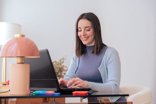 Happy Caucasian young student studying on her laptop in a home workspace. She looks focused and motivated, making this image ideal for online learning, education, remote studying, and academic success