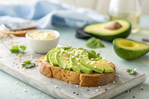 Freshly made avocado toast is served on a rustic wooden board. The bread is topped with sliced avocado, sprinkled with sesame seeds and herbs.