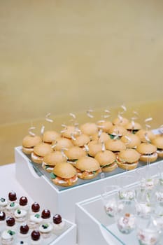 Mini burgers with salmon, small cakes and salads in glasses stand on a festive buffet. High quality photo