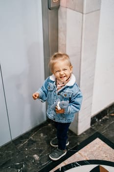 Little laughing girl stands with a toy in her hand near the elevator door. High quality photo