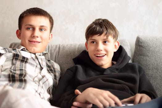 Portrait of two brothers sitting on a sofa and looking aside, listening attentively with admiration and smiling. High quality photo