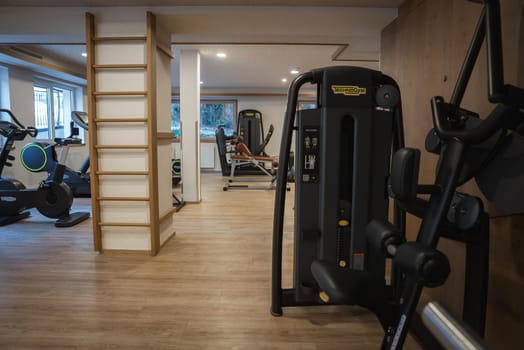 A well lit gym with Technogym machines, stationary bikes, wooden flooring, and a window offering a view of trees in Ischgl, Austria.