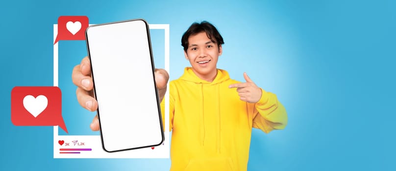 A young influencer in a bright yellow hoodie holds up a smartphone, pointing at the blank screen. The background is a vibrant blue, highlighting social media elements like hearts and chat bubbles.