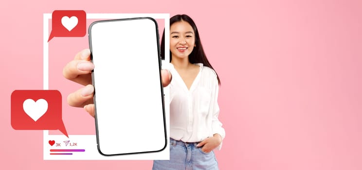 An influencer smiles while holding a blank smartphone in front of a pink background, highlighting social media engagement elements like hearts and chat bubbles, perfect for online content promotion.