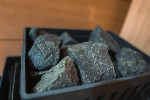 Dark, rough textured stones in a black vented container, set against wooden paneling, suggest a sauna in a luxury resort in Ischgl, Austria.