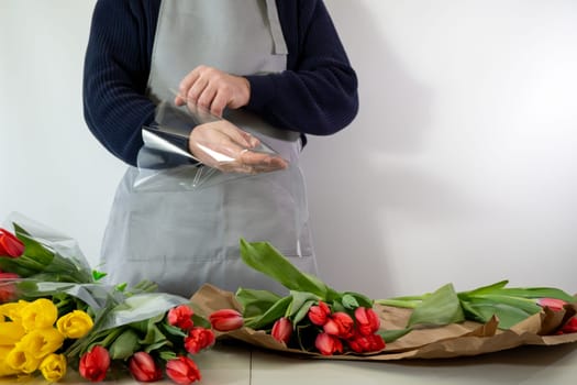 Caucasian male florist arranging tulip bouquets in apron.