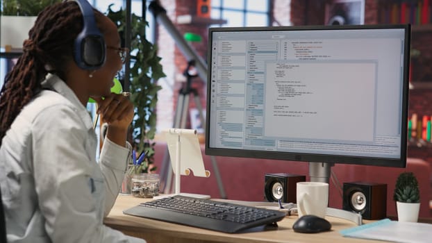 Jolly engineer in home office working on computer, dancing at desk in celebration after successfully executing code. IT worker wearing headphones happy after finishing compiling code, camera B