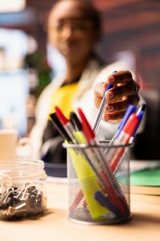 Woman in home office reaching for pencil from desk organizer, preparing to jot down important notes. Person taking pencil from workspace stationary holder to do writing, close up