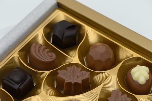Exquisite handcrafted chocolates showcase intricate designs within a golden box. Each piece varies in shape and flavor, inviting indulgence and delight on a special occasion.