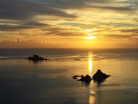 Bright orange sun rising over the beach town of Oakura, New Zealand. Silhouetted rocky islands and outlets frame the serene and tranquil scene