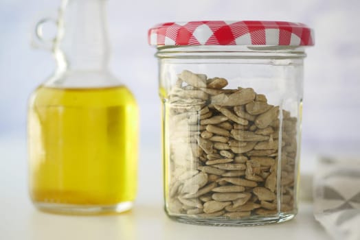 A jar filled with sunflower seeds sits next to a bottle of oil.