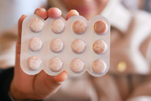 Person displays a blister pack containing round tablets indoors.