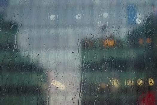 Raindrops trickle down a window, obscuring the cityscape behind.