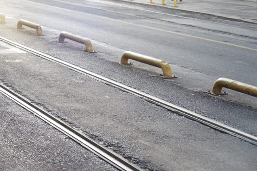 Metal tracks run parallel to yellow barriers on a calm city road.