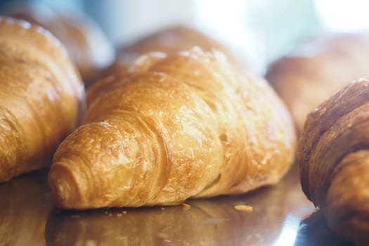 Warm, flaky croissants rest on a shiny surface in the bakery's morning light.