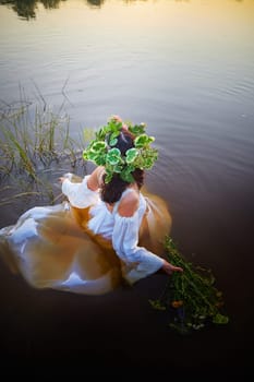 Slavic plump chubby girl in long white dress on the feast of Ivan Kupala with flowers and water in a river or lake on summer evening