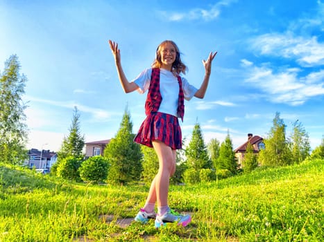 A young girl joyfully dances in a lush green park surrounded by trees and suburban houses, basking in bright daylight.