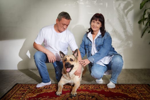 Middle-aged couple poses with their friendly German shepherd in their charming apartment, capturing a moment of love and togetherness.