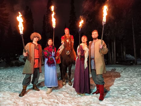 Actors in traditional costumes perform a captivating fire show under winter night skies, showcasing bravery and tribal spirit.