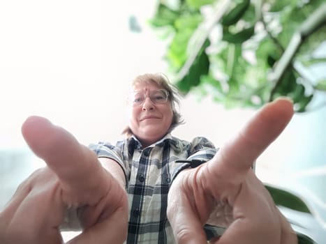 Blonde woman enjoys a moment of self-expression by taking a cheerful selfie, surrounded by greenery in her cozy living space.